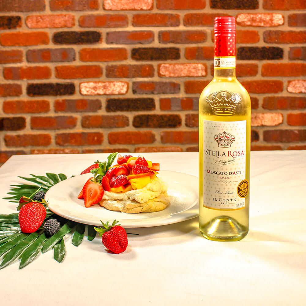 Pastel de Pavlova con frutas servido en un plato blanco junto a una botella de Moscato d'ASti.