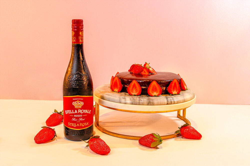 Pastel de terciopelo rojo con fresas frescas, servido en un soporte de pastel de granito con Stella Rosa Royale.